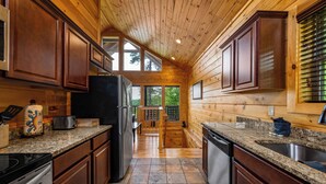 A kitchen with wooden cabinets, granite countertops, a refrigerator, and a dishwasher.