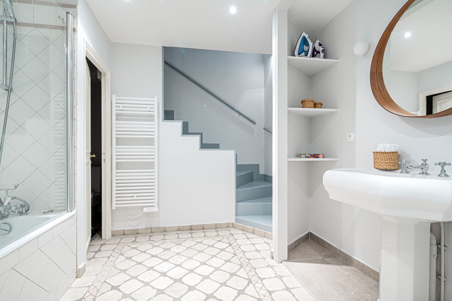 A bathroom with a white sink, a mirror, and a staircase leading to another room.