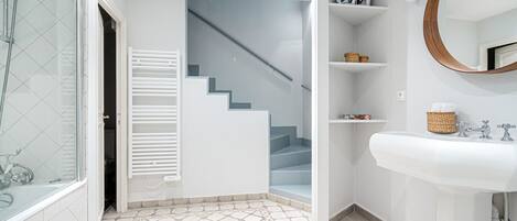 A bathroom with a white sink, a mirror, and a staircase leading to another room.