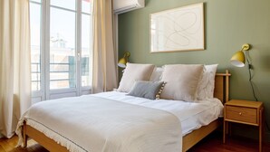 A bedroom with a bed, two bedside lamps, a wall-mounted air conditioner, and a window with curtains. - Blueground | Faisanderie, a/c, nr Eiffel Tower (Paris)