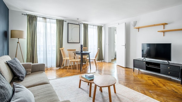 A modern living room with a sofa, dining table, chairs, a TV, and a floor lamp. - Blueground | Saint Germain, nr the Sorbonne (Paris)