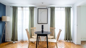 A room with a round table, four wooden chairs, a floor lamp, and a framed artwork on the wall. - Blueground | Saint Germain, nr the Sorbonne (Paris)
