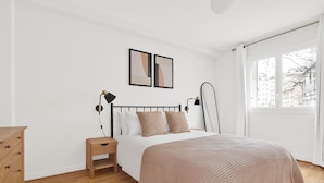 A bedroom with a bed, bedside tables, a dresser, and a window with a view of buildings. - Blueground | Auteuil, elevator & concierge (Paris)