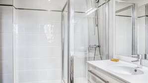 A modern bathroom with a glass-enclosed shower, a white sink with a mirror, and a wooden floor. - Blueground | Miromesnil, nr Parc Monceau (Paris)
