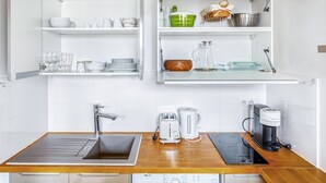 A modern kitchen with white cabinetry, a stainless steel sink, a coffee maker, and a kettle. - Blueground | Miromesnil, nr Parc Monceau (Paris)