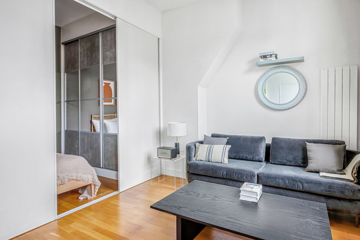 A modern living room with a grey sofa, a coffee table, a lamp, and a large mirror on the wall.