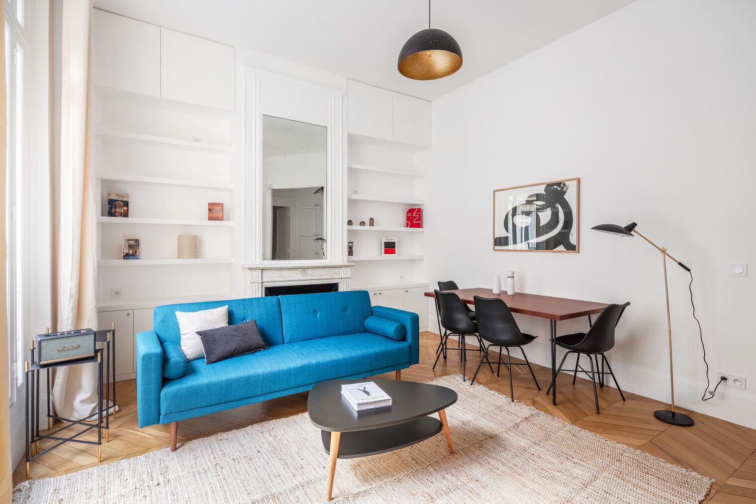 Ein modernes Wohnzimmer mit blauem Sofa, Couchtisch, Essbereich mit Stühlen, Kamin und einem großen Spiegel.