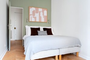 Ein Schlafzimmer mit Bett, einer Tür und einem an der Wand befestigten abstrakten Kunstwerk.