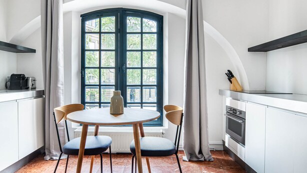 Eine Küche mit rundem Tisch, zwei Stühlen, einem Fenster mit Vorhängen und einem Herd.