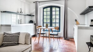 Eine moderne Küche mit Essbereich, einem großen Fenster mit Vorhängen und einer Couch mit gemusterten Kissen.