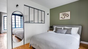 Ein Schlafzimmer mit einem großen Bett, einem Spiegel, einem Nachttisch und einer Wandleuchte.