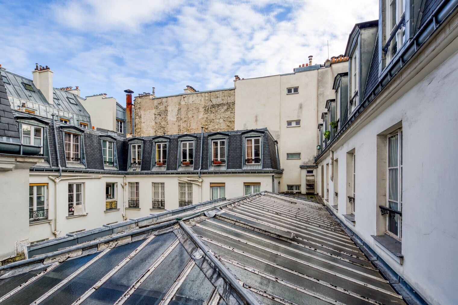 A narrow street with buildings on both sides, featuring multiple windows and a visible rooftop.