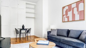 Ett modernt vardagsrum med en grå soffa, ett matbord med stolar, ett soffbord med böcker och en stor, abstrakt tavla på väggen.