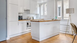 A modern kitchen with white cabinetry, a wooden countertop, and a central island. - Blueground | Arc de Triomphe, nr shops (Paris)