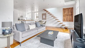 A modern living room with a grey sofa, a coffee table, and a TV. There is a staircase leading to an upper floor. - Blueground | Arc de Triomphe, nr shops (Paris)