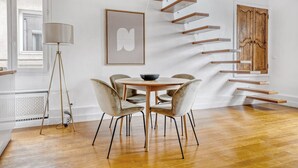 A modern interior with a wooden dining table, chairs, a floor lamp, a staircase with wooden steps, and a framed artwork on the wall. - Blueground | Arc de Triomphe, nr shops (Paris)