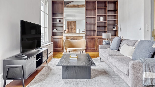 A modern living room with a television, sofa, coffee table, and built-in wooden shelving. - Blueground | Arc de Triomphe, nr shops (Paris)