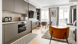 Une cuisine moderne dotée d’appareils électroménagers intégrés, un coin repas avec une table ronde et des chaises, et un balcon avec vue.