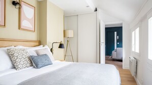Une chambre avec un grand lit, une lampe de chevet et une vue sur un couloir menant à la salle de bain.