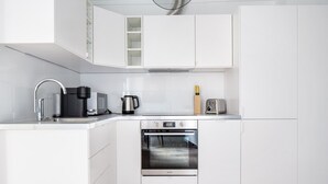 Une cuisine moderne avec des meubles blancs, un four en acier inoxydable, une machine à café, une bouilloire et un grille-pain.