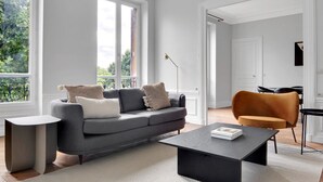 Una sala moderna con un sofá gris, una mesa de centro negra y un sillón de color mostaza.