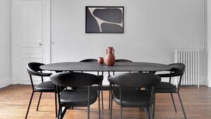Una mesa redonda de comedor con seis sillas negras, un jarrón y un cuadro abstracto enmarcado en la pared.