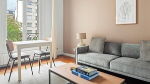 A living room with a grey sofa, a white table with chairs, a lamp, and a framed abstract artwork on the wall. - Blueground | Arc de Triomphe, nr Parc Monceau (Paris)