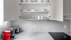 A kitchen with white cabinets, a red coffee machine, and a black induction cooktop. - Blueground | Montparnasse, furnished & equipped (Paris)