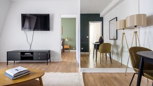 A modern living room with a flat-screen TV, a dark wooden entertainment unit, a round coffee table with books, and a view into a dining area with a table and chairs. - Blueground | Champs de Mars, elev, nr Eiffel Tower (Paris)