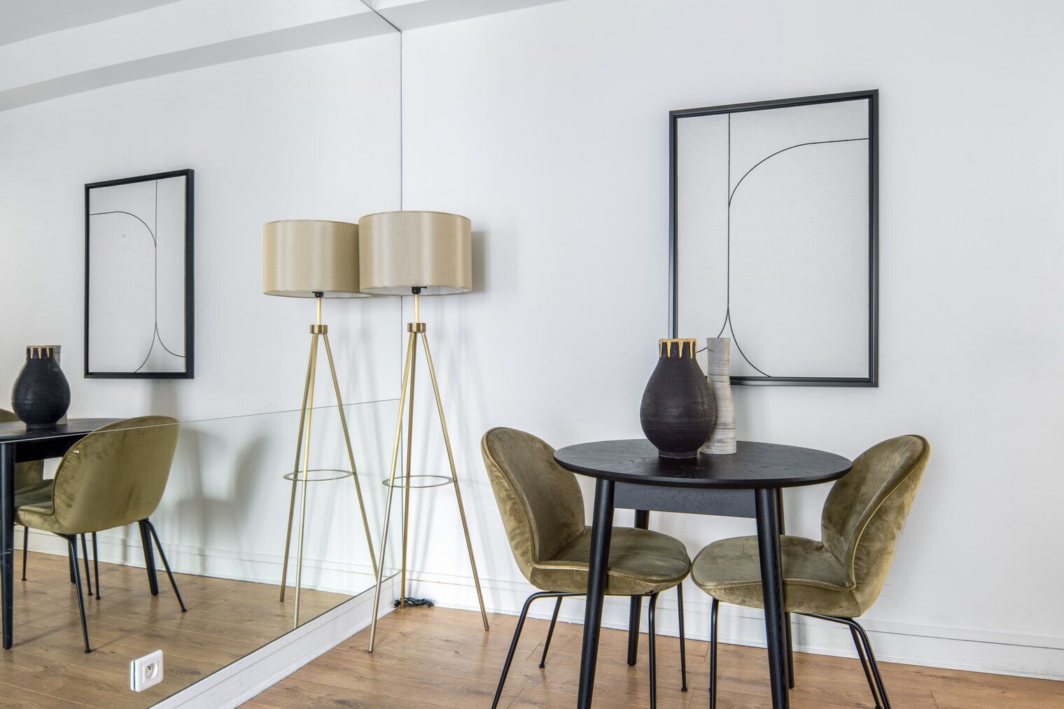 Un interior moderno con una mesa redonda, dos sillas, una lámpara de pie y dos obras de arte abstracto enmarcadas en la pared.