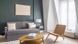 A modern living room with a grey sofa, a wooden coffee table, a side table with a lamp, and a large window with sheer curtains. - Blueground | Champs de Mars, elev, nr Eiffel Tower (Paris)