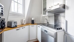 A compact kitchen with white cabinets, a stainless steel dishwasher, a coffee maker, and a toaster. - Blueground | Champs de Mars, elev, nr Eiffel Tower (Paris)
