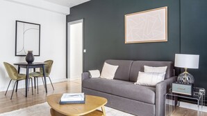 A modern living room with a grey sofa, a round wooden coffee table, and a dining area with two chairs. - Blueground | Champs de Mars, elev, nr Eiffel Tower (Paris)