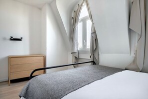 Une chambre à coucher avec un lit, une commode en bois et une fenêtre avec des rideaux.