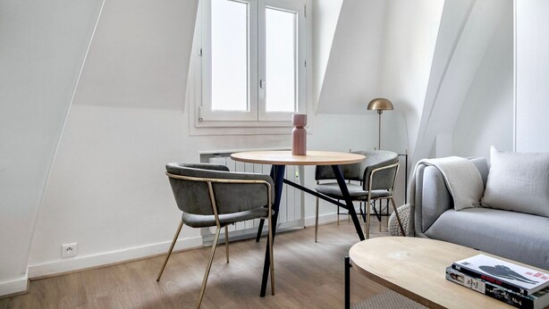 A modern loft bedroom with a sloped ceiling, a round dining table, two chairs, a sofa, and a floor lamp. - Blueground | Montorgueil, concierge, furnished (Paris)