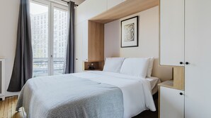 A modern bedroom with a large bed, a wooden headboard, a bedside table, and a framed artwork on the wall. - Blueground | Trocadero, elevator, nr Eiffel Tower (Paris)