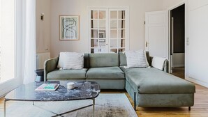 A modern living room with a green sectional sofa, a glass coffee table, and a framed artwork on the wall. - Blueground | Trocadero, elevator, nr Eiffel Tower (Paris)