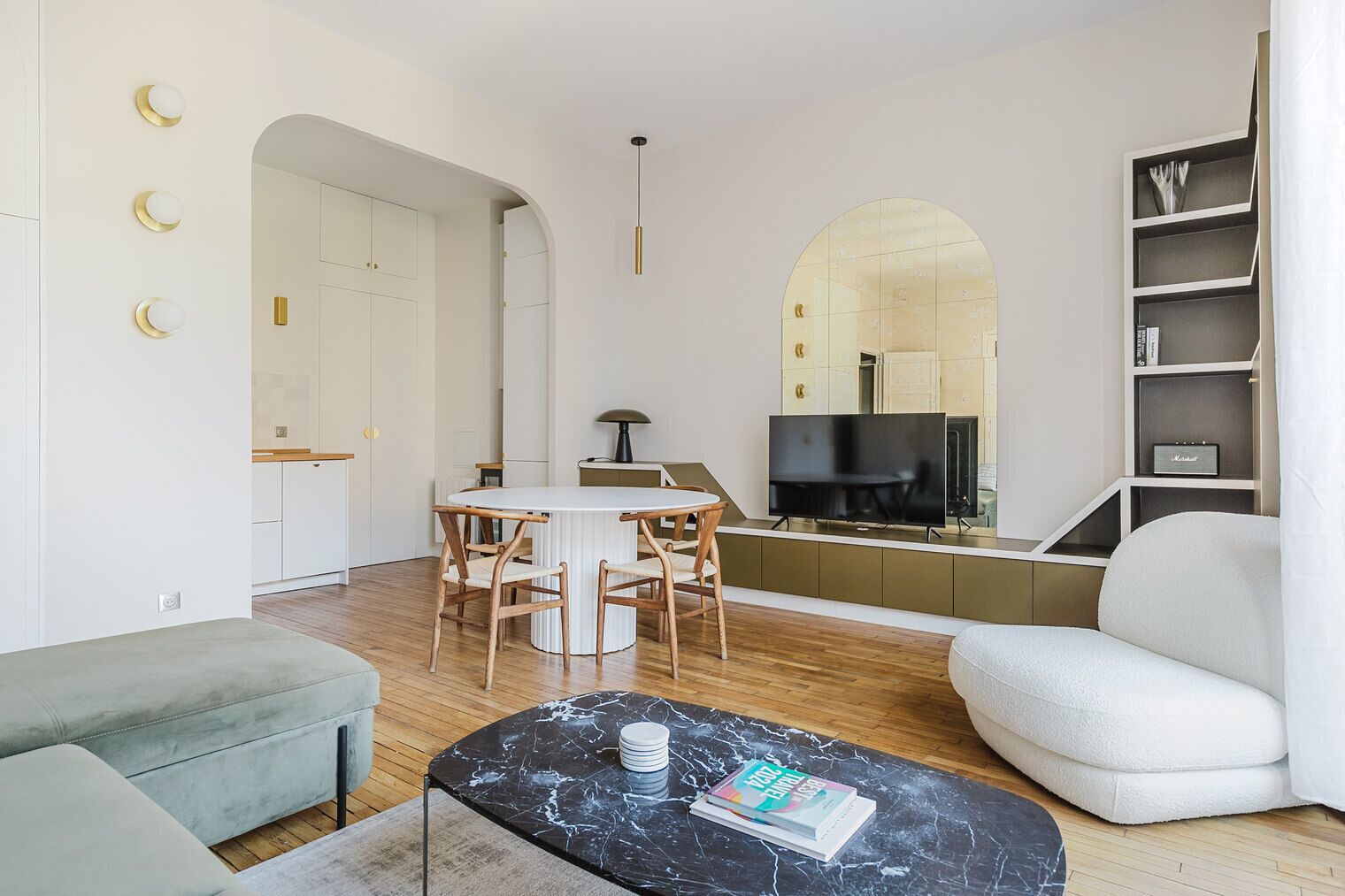 A modern living room with a round dining table, two sofas, a marble coffee table, and a television in the background.