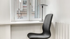 A modern chair with a high backrest placed next to a window with a view of a building.