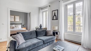 Un salon moderne avec un canapé gris, une table basse et un lit dans la pièce adjacente.