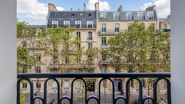 Une vue d’une rangée de bâtiments historiques dotés de balcons, avec un ciel dégagé et des arbres au premier plan.