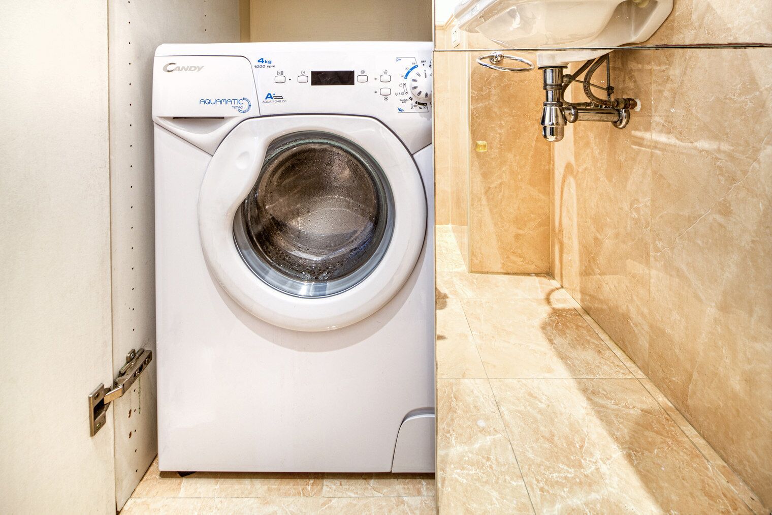 A compact, modern washing machine in a small bathroom with a marble floor and a sink.