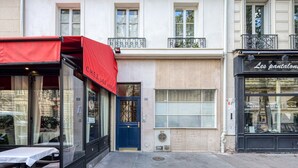 Un bâtiment avec une porte bleue, un auvent rouge et une devanture de magasin sur laquelle on peut lire : « Les pantaloons ».