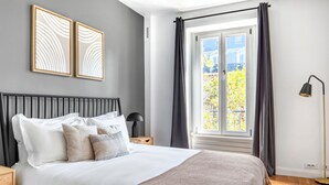 Une chambre à coucher avec un lit, une table de chevet, une lampe et une fenêtre avec des rideaux.