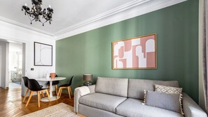 Un salon moderne avec un mur d’accent vert, un canapé gris et un coin repas comprenant une table blanche et des chaises noires.