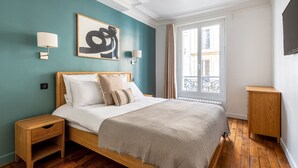 Une chambre avec un lit en bois, des murs de couleur turquoise, une grande fenêtre et un téléviseur fixé au mur.