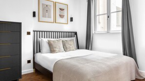 A neatly arranged bedroom with a bed, a dresser, and two framed artworks on the wall.