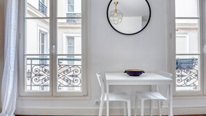 Une pièce avec une table et des chaises blanches, un grand miroir rond accroché au mur et une vue sur des balcons à travers de grandes fenêtres.