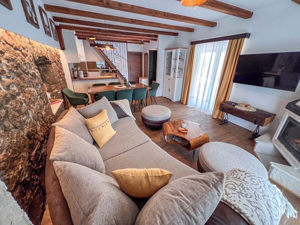 Una sala de estar con un sofá, un reposapiés y una mesa de centro de madera. Hay una zona de comedor con sillas y una mesa, y una cocina al fondo.
