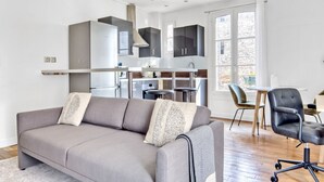A modern living room with a grey sofa, a dining table with chairs, and a kitchen area with stainless steel appliances. - Blueground | Bastille, elevator, nr Charonne (Paris)